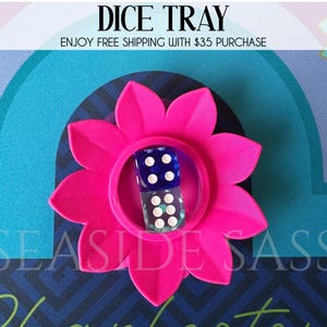 May include: A hot pink flower-shaped dice tray with two dice inside. The dice are blue and clear with white dots. The text "DICE TRAY" is at the top of the image, and "SEASIDE SASS" is at the bottom.