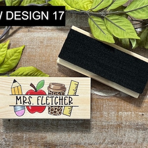 May include: Wooden teacher desk organizer with the text "MRS. FLETCHER" and school-themed illustrations. Includes a pencil, apple, coffee cup, and ruler. A separate wooden eraser is also present. The text "NEW DESIGN 17" is in the upper left corner.