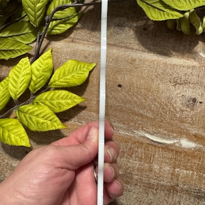 Pu&ograve; includere: Un sottile pezzo rettangolare in acrilico bianco con angoli arrotondati, visto di profilo. L'oggetto presenta una superficie bianca liscia e solida con uno spessore uniforme, mostrando un bordo verticale netto orientato verso l'alto.