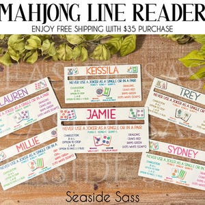 May include: Mahjong Line Readers with player names, game instructions, and tile illustrations. Each reader is rectangular, with a white background and colorful text. The readers are arranged on a wooden surface with green foliage.