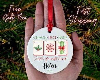 May include: A white ceramic Christmas ornament with a red ribbon. The ornament features the text "CRACK DOT BAM" and "Santa's favorite hand". It displays three Mahjong tiles with holly, a peppermint candy, and bamboo. The name "Helen" and the year "2025" are also printed.
