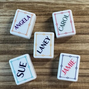 May include: Five rectangular white tiles with rounded corners, each featuring a colored border and a name printed in the center. The names are Angela in purple, Carol in dark green, Laney in black, Sue in dark blue, and Jamie in red.