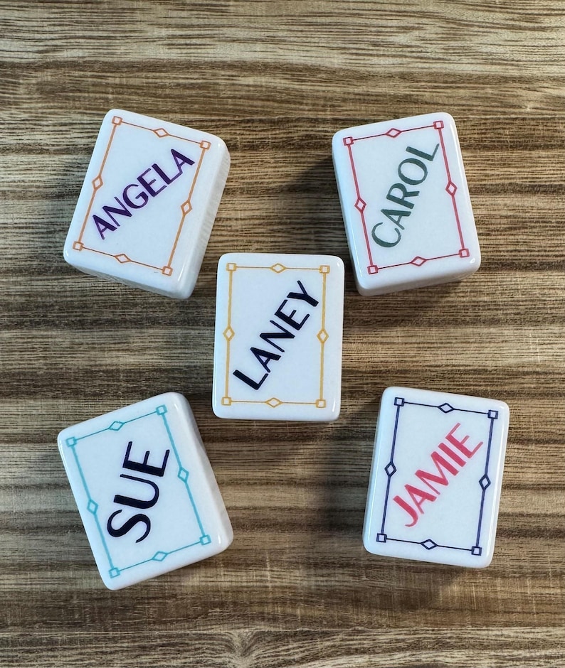 May include: Five rectangular white tiles with rounded corners, each featuring a colored border and a name printed in the center. The names are Angela in purple, Carol in dark green, Laney in black, Sue in dark blue, and Jamie in red.