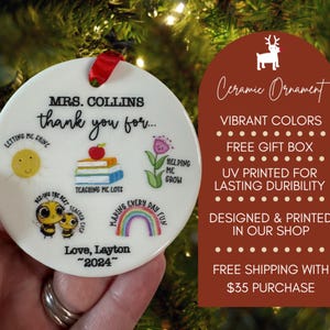 May include: A white ceramic ornament with a red ribbon, featuring colorful illustrations and text. The ornament says "Mrs. Collins, thank you for..." with drawings of a sun, books, a flower, a rainbow, and bees. The text also includes "Love, Layton ~2024~."