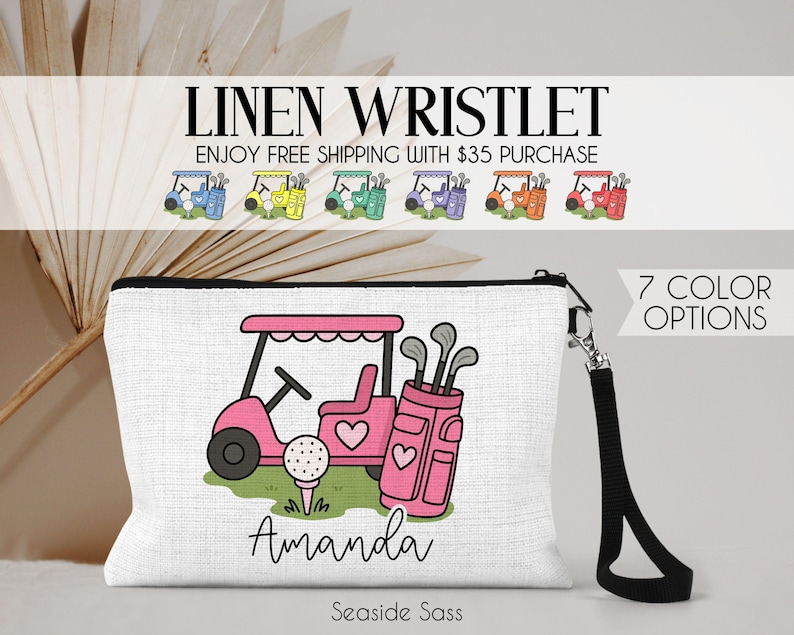 May include: White linen wristlet with a black zipper and wrist strap. The design features a pink golf cart, golf bag, and golf ball. The name "Amanda" is printed below the golf scene. The text "LINEN WRISTLET" and "7 COLOR OPTIONS" are also visible.