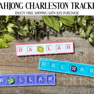May include: Three Mahjong Charleston Tracker boards in pink, blue, and purple. Each board has the letters R, A, L, and R, with a die in the center. The text "MAHJONG CHARLESTON TRACKER" is at the top.
