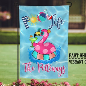 May include: A blue and white garden flag with a pink flamingo holding a green drink. The flag says "Pool Life" and "The Petteways".