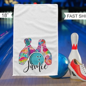 May include: White towel with a colorful bowling pin design and the name "Jamie" written in black cursive. The towel is 11 inches by 18 inches.