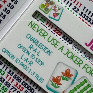 Pu&ograve; includere: Primo piano di una carta da Mahjong con il testo "NEVER USE A JOKER FOR". La carta presenta illustrazioni di tessere colorate e combinazioni di numeri. La carta &egrave; bianca con testo verde, rosso e nero.