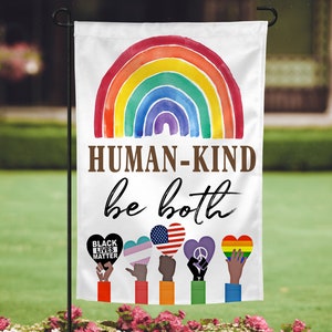 May include: A white garden flag with a rainbow arch and the text "HUMAN-KIND be both".  Below the text are six hands holding hearts with different symbols, including a black fist with the text "BLACK LIVES MATTER", a transgender symbol, an American flag, a peace sign, and a rainbow heart.