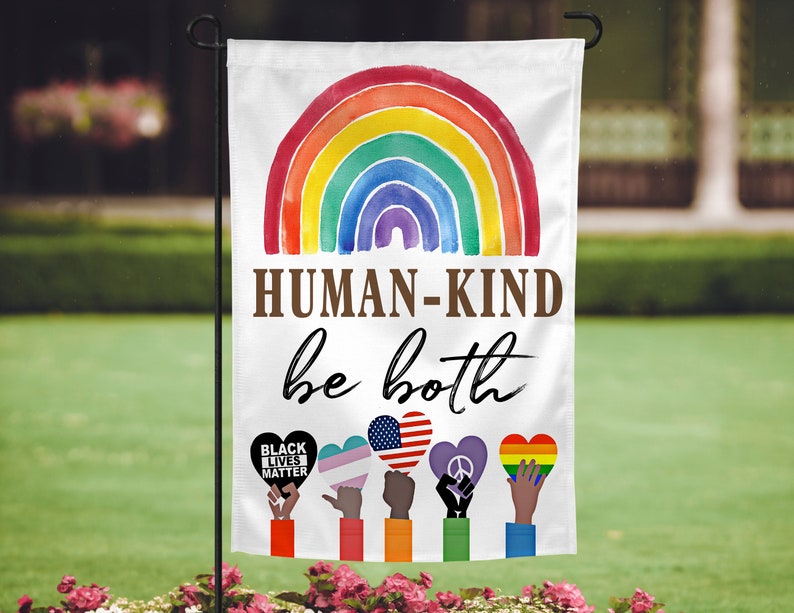 May include: A white garden flag with a rainbow arch and the text "HUMAN-KIND be both".  Below the text are six hands holding hearts with different symbols, including a black fist with the text "BLACK LIVES MATTER", a transgender symbol, an American flag, a peace sign, and a rainbow heart.