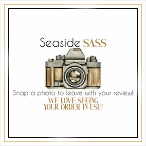May include: A white card with a black border and gold text that says "Seaside SASS". A vintage camera with a brown leather case is in the center of the card. The text below the camera says "Snap a photo to leave with your review! WE LOVE SEEING YOUR ORDER IN USE!"