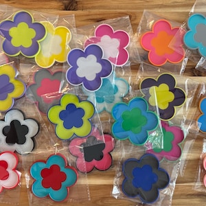 K&ouml;nnte beinhalten: Eine Sammlung bunter, bl&uuml;tenf&ouml;rmiger Untersetzer in verschiedenen Farben, darunter Rosa, Blau, Gelb und Orange. Jeder Untersetzer ist in einer transparenten Plastikt&uuml;te verpackt. Die Untersetzer sind aus strapazierf&auml;higem Material.