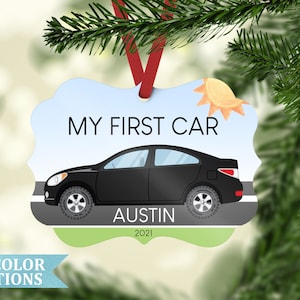 May include: A decorative ornament with the text "MY FIRST CAR" and a black car illustration. The ornament includes the name "Austin" and the year "2021". The ornament has a red ribbon for hanging.