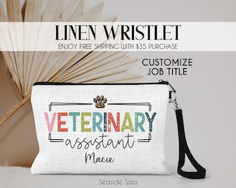 May include: A white linen wristlet with a black zipper and a black wrist strap. The wristlet has a colorful graphic that says "Veterinary Assistant Macie".