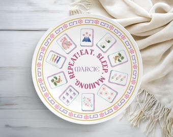 May include: White ceramic plate with a gold and pink floral border. The plate features illustrated Mahjong tiles and the words "REPEAT! EAT. SLEEP. MAHJONG. MARIE" in pink and purple.