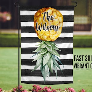 May include: A black and white striped garden flag with a pineapple illustration. The pineapple is yellow and green and has the text "The Wilsons" on it.