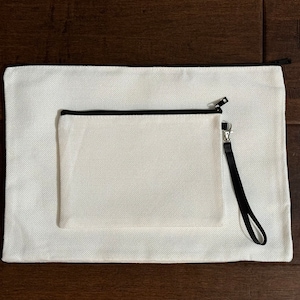 May include: Two white canvas pouches with black zipper pulls and black trim. The smaller pouch has a black strap.