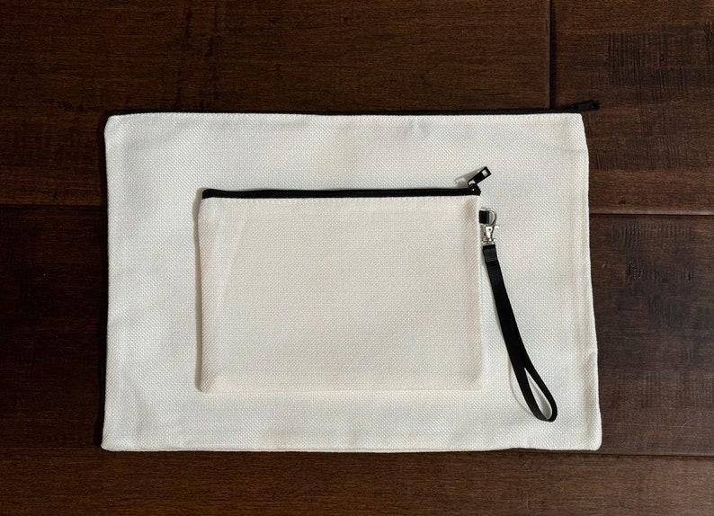 May include: Two white canvas pouches with black zipper pulls and black trim. The smaller pouch has a black strap.