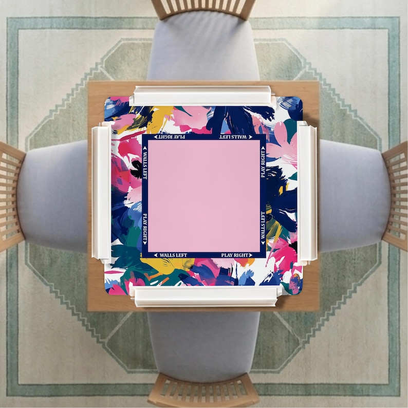 May include: A square mahjong mat featuring a vibrant, abstract floral pattern in shades of navy blue, pink, yellow, and white. The center contains a solid pink square bordered by a navy frame with the text WALLS LEFT and PLAY RIGHT printed.