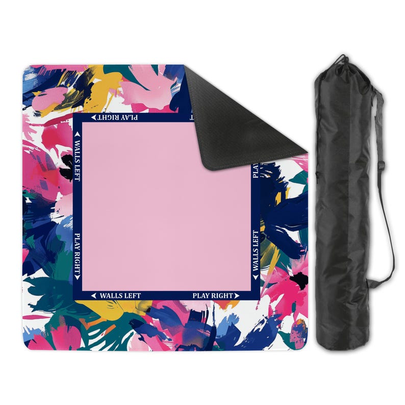 May include: A square mat featuring a vibrant abstract floral pattern in pink, blue, yellow, and white, with a central solid pink square bordered by dark blue text reading WALLS LEFT and PLAY RIGHT, accompanied by a black cylindrical carrying bag.