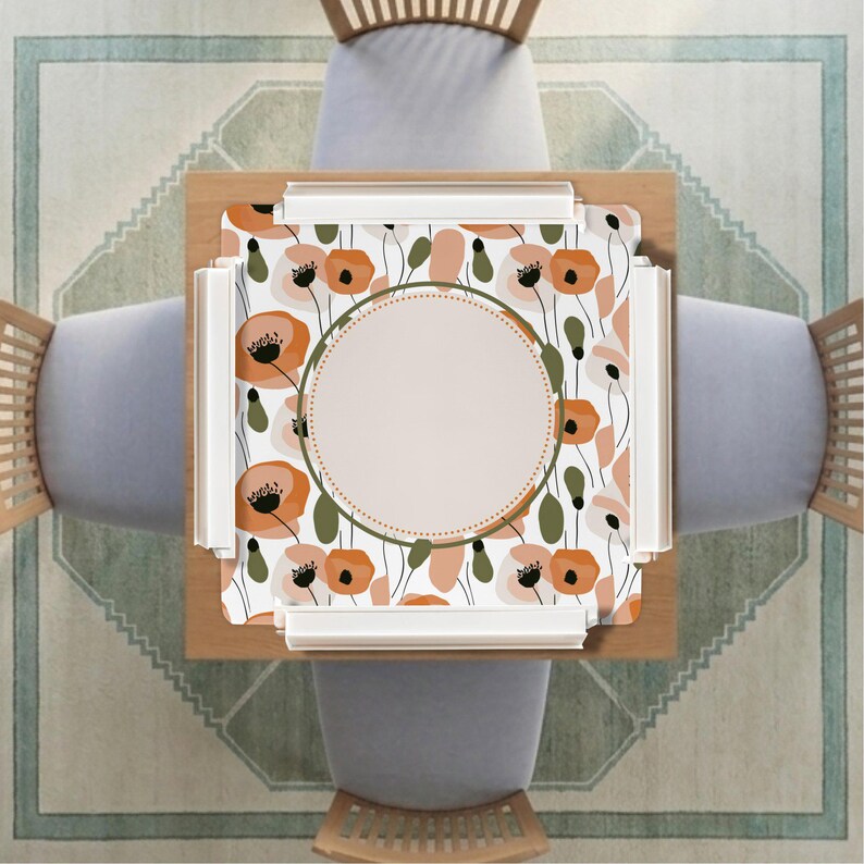 May include: A square table mat featuring a repeating pattern of orange and muted green poppy flowers on a white background. A large, solid beige circle is centered on the mat, framed by a thin dark green border with a dotted inner edge detail.