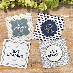 Peut inclure: Quatre sous-verres carr&eacute;s avec des motifs et du texte distincts. L'un est gris avec un motif de feuilles et indique LAST DISCARDED TILE. Un autre est bleu marine avec des demi-cercles blancs et indique LAST DISCARD. Deux autres ont des fonds blancs avec des bordures g&eacute;om&eacute;triques noires et le texte LAST DISCARD.