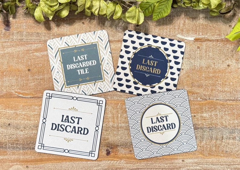 Peut inclure: Quatre sous-verres carr&eacute;s avec des motifs et du texte distincts. L'un est gris avec un motif de feuilles et indique LAST DISCARDED TILE. Un autre est bleu marine avec des demi-cercles blancs et indique LAST DISCARD. Deux autres ont des fonds blancs avec des bordures g&eacute;om&eacute;triques noires et le texte LAST DISCARD.
