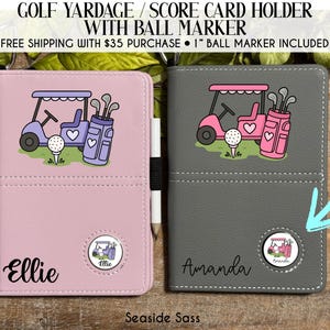 May include: Two golf yardage/score card holders. One is light pink with a golf cart graphic and the name "Ellie". The other is gray with a golf cart graphic and the name "Amanda". Each has a matching ball marker. Text on top reads "GOLF YARDAGE / SCORE CARD HOLDER WITH BALL MARKER".