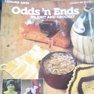 May include: A vintage magazine cover titled "Odds 'n Ends To Knit and Crochet" features a glass of red wine, bread, and a bowl of soup. The cover also showcases various knitted and crocheted items, including a yellow and white potholder and a pair of red slippers.