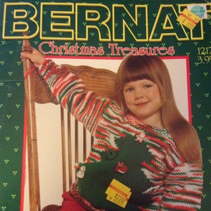 May include: A girl wearing a red, white, and green striped sweater with a Christmas tree design. The sweater has a green, white, and red striped trim. The girl is sitting on a wooden chair. The sweater has a price tag that says "Clearance $1.50".