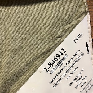 May include: A close-up of a green fabric swatch with a white label attached. The label has the text "2-846942", "Railroad Random, Pattern Code: A", "Dyelot may vary slightly from this sample", "100% Polyester", "Cleaning Code: W", "Treated", "Repeat = None", "UFAC 1", and "Twillo".