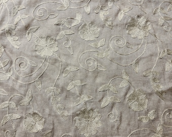 May include: A beige fabric with a delicate floral embroidery pattern in a light gray color. The design features stylized flowers and leaves.