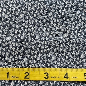 May include: A close-up of a dark blue fabric with a white floral pattern. A yellow measuring tape with the text "60 in" and "Made in China" is placed on top of the fabric.