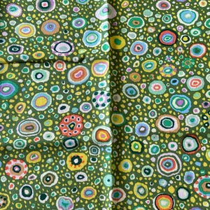 Peut inclure: Gros plan sur un tissu vert avec un motif répété de cercles abstraits colorés. Les cercles sont dans des tons de jaune, orange, bleu et blanc, avec de petits points dispersés. Le tissu a un aspect texturé.