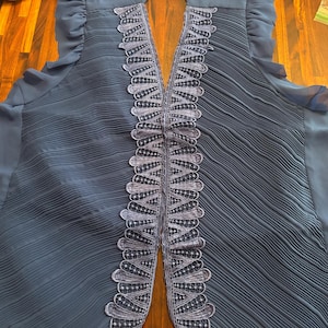 May include: A navy blue vest with a pleated design. The vest features a decorative, scalloped trim in a lighter shade of blue along the front opening. The vest has a flowing, lightweight appearance.