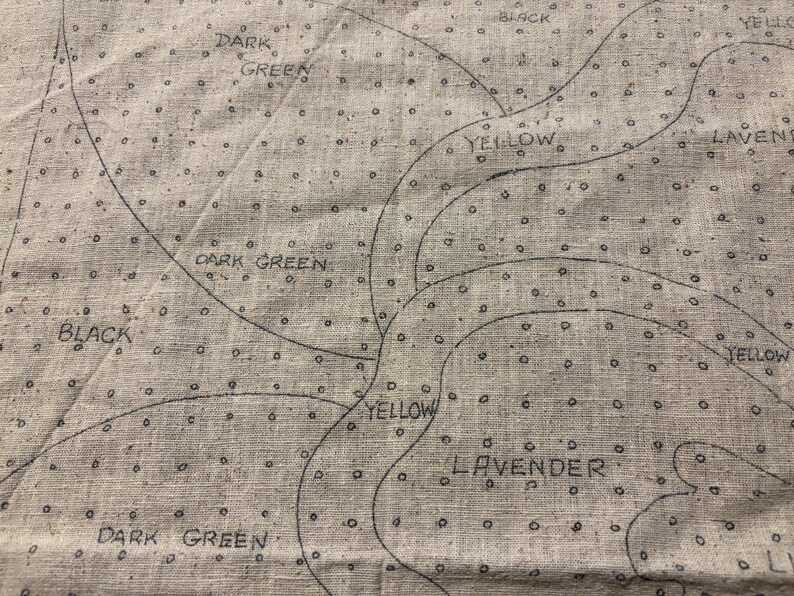 May include: A close-up of a beige fabric with black lines and dots. The fabric is labeled with the words "Dark Green", "Yellow", "Lavender", and "Black".