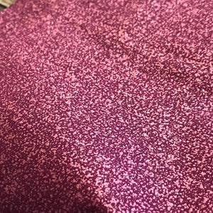 Pode incluir: Close-up de um tecido rosa escuro com um brilho sutil. O tecido tem uma aparência texturizada e salpicada.