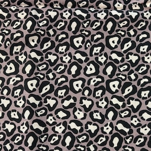 Puede incluir: Primer plano de una tela con estampado de leopardo. El diseño presenta manchas negras con centros blancos sobre un fondo malva. La tela se utiliza probablemente para ropa o decoración del hogar.