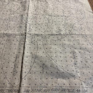 May include: A close-up of a beige fabric with a printed pattern of a flower. The pattern is outlined in black and includes the words "Yellow", "Lavender", "Black", "Dark Green", and "Use 'Star' rug yarn article 44 or 'Lydia's heavy rug yarn article 235 can be used."