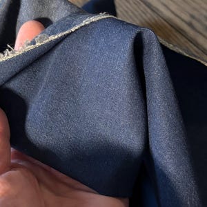 May include: Close-up of dark blue denim fabric, folded to show texture and the raw edge. The denim has a classic, slightly worn look. Suitable for various sewing projects, the fabric is a deep, rich blue.