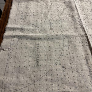 May include: A close-up of a beige canvas with a black and white design for a rug. The design includes a variety of shapes and lines, with the words "PANSY DESIGN N№ 523 RUG SIZE 24&times;36 AMERICAN USE STAR COTTON YARN ARTICLE 15 ALSO AUNT" printed at the bottom.