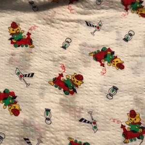 May include: White fabric with a repeating pattern of red, green, and yellow toy trains with cats on them. There are also small black and white traffic lights and blue and white lanterns.