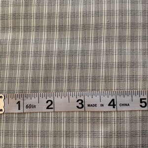 Peut inclure: Gros plan sur un tissu blanc à motif à carreaux noir et blanc. Un mètre ruban est placé sur le tissu, montrant des mesures de 1 à 5 pouces.