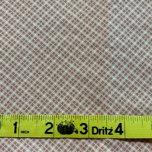 Könnte beinhalten: Rosa-weiß karierter Stoff mit einem gelben Maßband. Das Band zeigt 2,5 cm bis 12,7 cm an. Der Stoff hat ein kleines, sich wiederholendes Gittermuster. Der Stoff hat eine hellrosa Farbe.