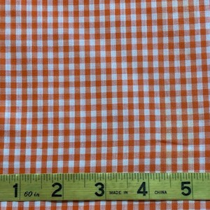 Può includere: Tessuto gingham arancione e bianco con un metro a nastro che mostra 15 cm.