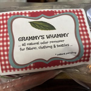 May include: A clear plastic bag containing a product label with the text "GRAMMY'S WHAMMY" and "... all natural odor remover for fabric, clothing & textiles ...". The label has a red and white checkered pattern and a green leaf illustration.