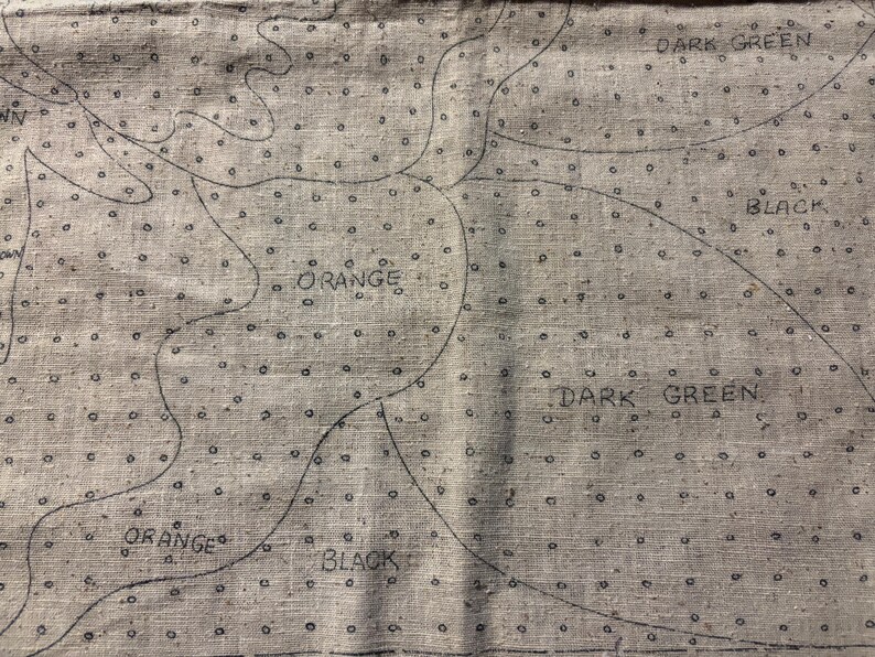 May include: A close-up of a fabric with a pattern of small circles and lines. The fabric is labeled with the words "Orange", "Black", and "Dark Green".