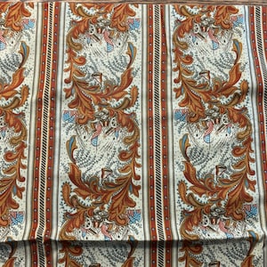 Może przedstawiać: Biała tkanina z powtarzającym się wzorem brązowych i pomarańczowych wzorów kwiatowych i niebieskich i czerwonych akcentów. Tkanina ma pasiasty wzór.