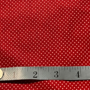 May include: Red fabric with a white polka dot pattern. A measuring tape is placed across the fabric, showing measurements in inches. The fabric is likely used for sewing or crafting projects.
